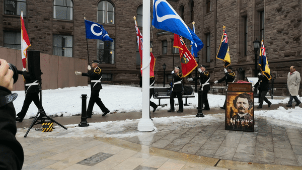People in uniform march while carrying flags.