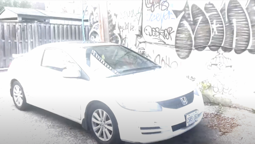 White Honda with graffiti wall behind.