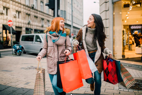 two women smiling and walking down the street with shopping bags