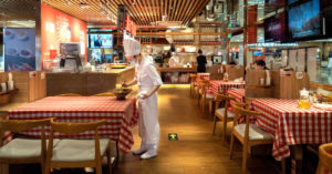 A mostly empty restaurant with a single chef and one guest at a table.