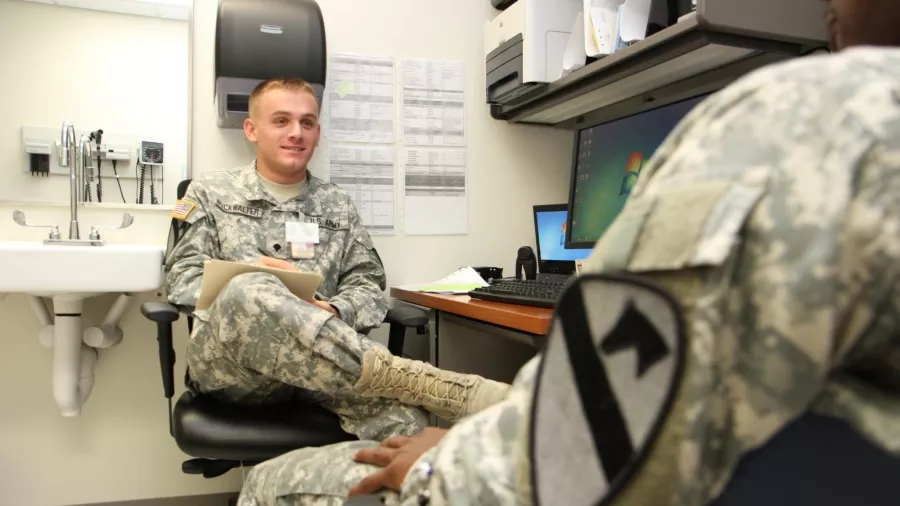 Soliders in a doctors office, talking while the medical advisor takes notes.