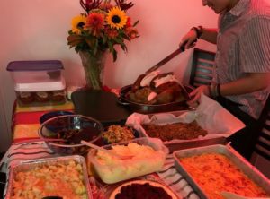 A young man is standing over several prepared dishes set out on a table decorated with flowers and a tablecloth