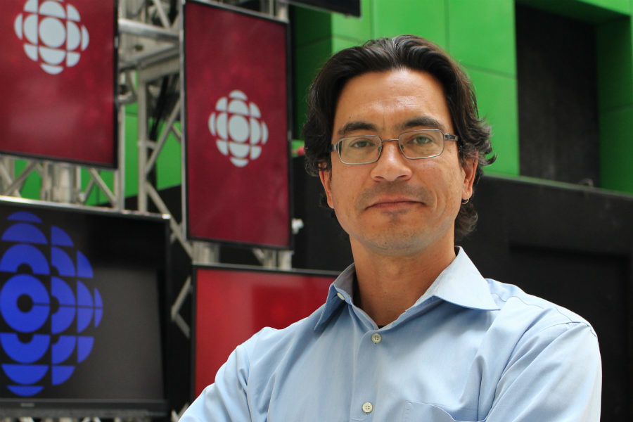 A man poses in front of TV screens that show the CBC logo.