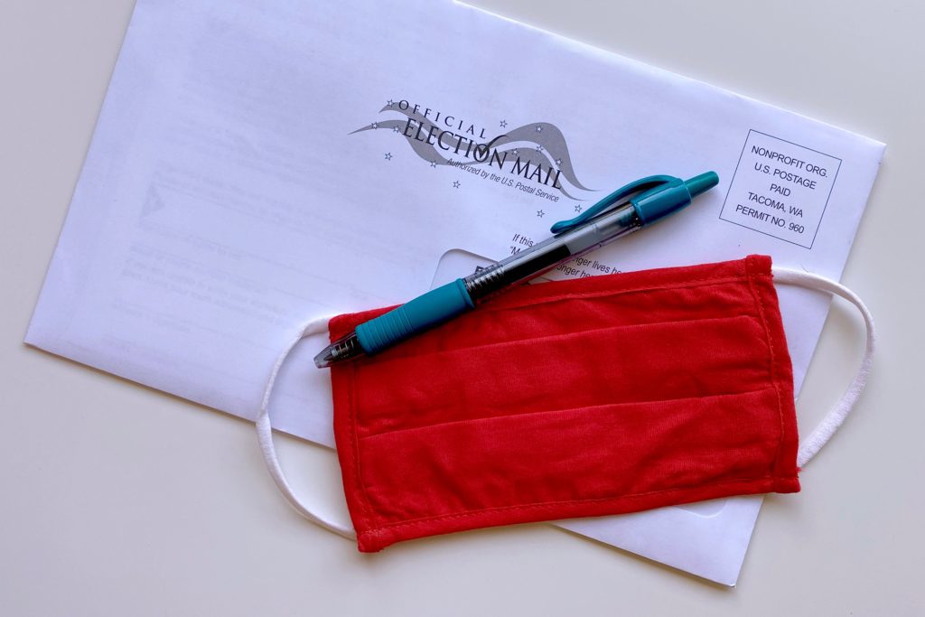 A red face mask and pen placed on top of an election envelope.