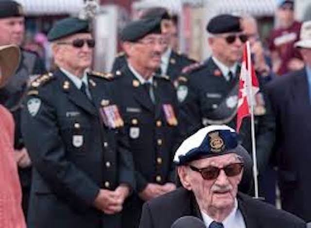 A group of war veterans attending an event, dressed in uniform. A Canadian flag is seen.