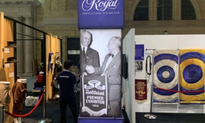 Photo of the 100th Royal Agricultural Winter Fair poster with a vintage photo of two men shaking hands. Fair booths surround the poster.